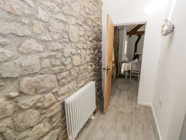 A hallway with a stone wall and white radiator leading to a dining area with a table and chairs at 1 Mountain View in Talwrn near Llangefni