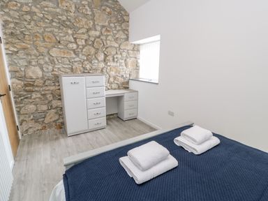A bedroom with a bed with folded towels on a blue blanket and a desk with drawers against a stone wall at 1 Mountain View in Talwrn near Llangefni