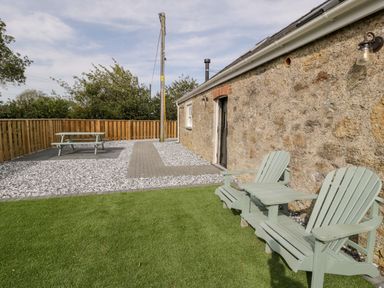 An outdoor patio area with two lounge chairs a picnic table and gravel surrounding a stone building at 1 Mountain View in Talwrn near Llangefni