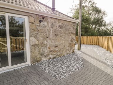 A stone exterior wall with glass sliding doors next to a paved pathway and wooden fence at 1 Mountain View in Talwrn near Llangefni
