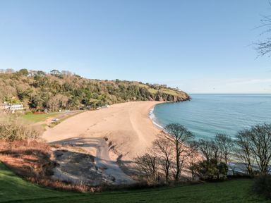 A beach with sand and water next to a wooded hillside at Yew Tree Cottage in Stoke Fleming