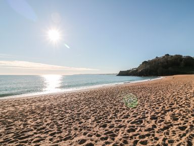 A sunny beach with footprints on the sand ocean waves and a hill with trees at Yew Tree Cottage in Stoke Fleming