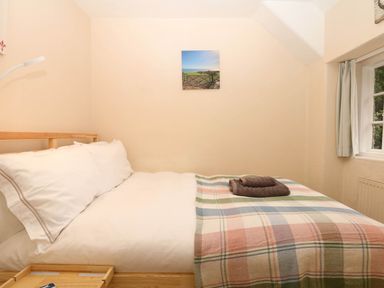 A bedroom with a bed, blanket, and lamp at Yew Tree Cottage in Stoke Fleming