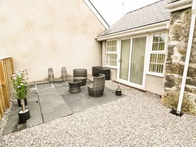 An outdoor patio area with three wicker chairs a wicker table potted flowers and gravel ground at 2 Mountain View in Talwrn near Llangefni