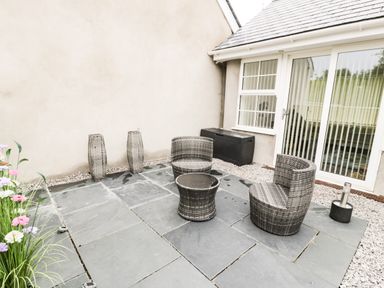 An outdoor patio with two wicker chairs and a small table near glass doors at 2 Mountain View Talwrn near Llangefni