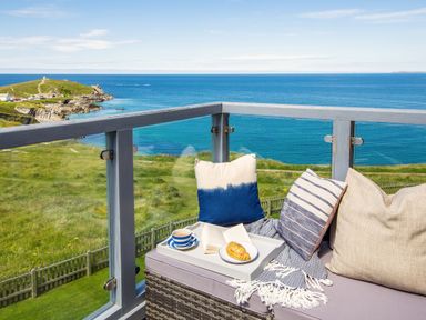 A balcony with cushions a tray with a cup an open book and a pastry overlooking the sea at Breakers in Newquay