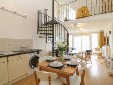 A dining area with a table set for four and flowers a spiral staircase and a living area with wicker chairs and a sofa at Breakers in Newquay
