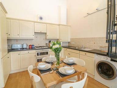 A kitchen with cream cabinets a dining table set for four and a washing machine at Breakers in Newquay