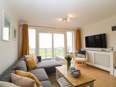 A living room with a grey sofa and yellow curtains overlooking a balcony at Breakers in Newquay