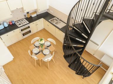A kitchen with cream cabinets black countertops a wooden dining table set with tableware and a black spiral staircase at Breakers in Newquay