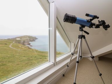 A telescope on a tripod next to a window with a view of a coastal landscape at Breakers in Newquay