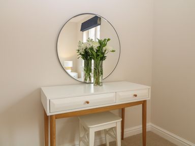 A white dressing table with wooden legs and a circular mirror with flowers in a glass vase at Breakers in Newquay