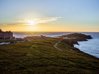 A coastal landscape with a grassy cliff path leading to buildings near the ocean at sunset at Breakers in Newquay
