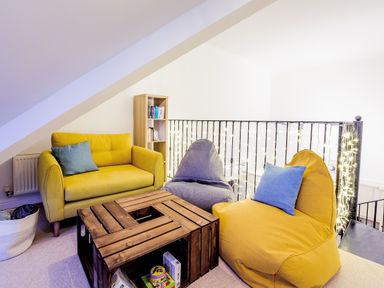 A small seating area with a yellow sofa and two bean bag chairs around a wooden crate table with books on a shelf at Breakers in Newquay