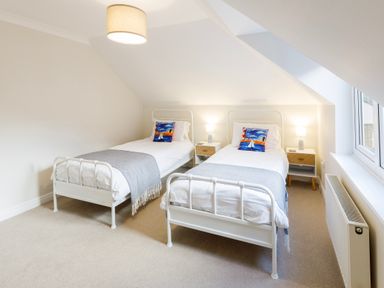 A bedroom with two single beds with white frames and colorful pillows at Breakers in Newquay