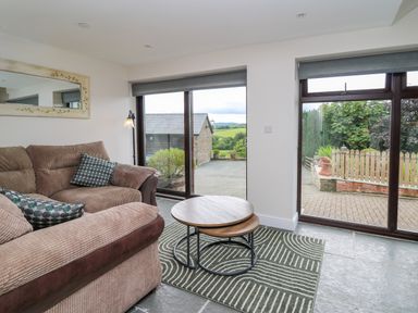 A living room with a corner sofa two nesting coffee tables and large windows overlooking an outdoor area at Cwmfadog in Llanafan-fawr near Beulah