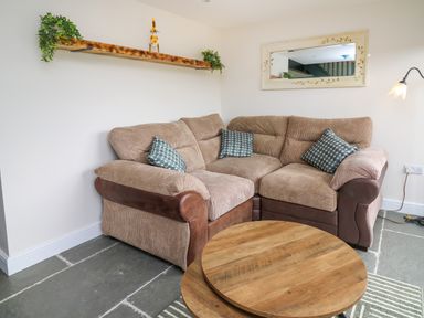 A corner sofa with cushions a round wooden coffee table and a wall shelf with plants in a living room at Cwmfadog in Llanafan-fawr near Beulah