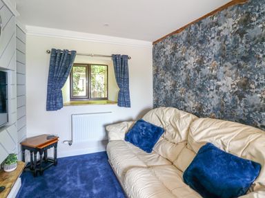 A living room with a cream sofa with blue cushions a small window with blue curtains and a small wooden table at Cwmfadog Llanafan-fawr near Beulah