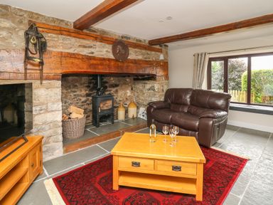 A living room with a stone fireplace wood burner leather sofa wooden coffee table with wine glasses and bottle on a red rug at Cwmfadog in Llanafan-fawr near Beulah