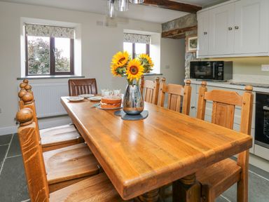A kitchen with a wooden dining table and chairs a vase of sunflowers and a cake on the table at Cwmfadog in Llanafan-fawr near Beulah