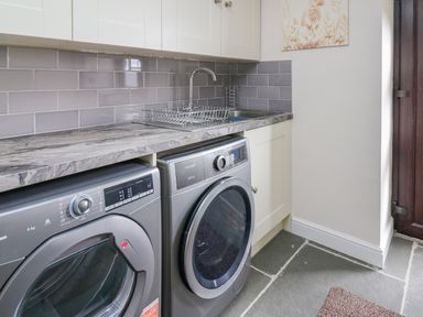 A laundry room with a washing machine and dryer under a countertop next to a sink at Cwmfadog in Llanafan-fawr near Beulah