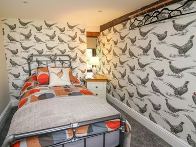 A small bedroom with a single bed patterned wallpaper and a bedside table with a lamp at Cwmfadog Llanafan-fawr near Beulah