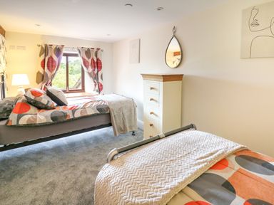 A bedroom with two single beds a chest of drawers a window with patterned curtains and a wall mirror at Cwmfadog in Llanafan-fawr near Beulah