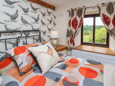 A bedroom with patterned bedding and wallpaper and a window with curtains at Cwmfadog in Llanafan-fawr near Beulah