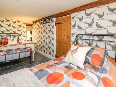 A bedroom with two metal beds patterned wallpaper with birds wooden door bedside table with lamp and hangers on the wall at Cwmfadog in Llanafan-fawr near Beulah
