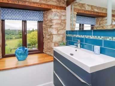 A bathroom sink with blue tiles and stone walls near a window with a blue vase on the wooden sill at Cwmfadog in Llanafan-fawr near Beulah