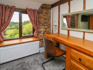 A room with a wooden desk and chair next to a window with red curtains at Cwmfadog in Llanafan-fawr near Beulah