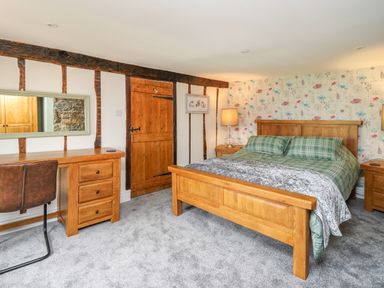 A bedroom with a wooden bed green plaid bedding wooden desk chair door and floral wallpaper at Cwmfadog in Llanafan-fawr near Beulah