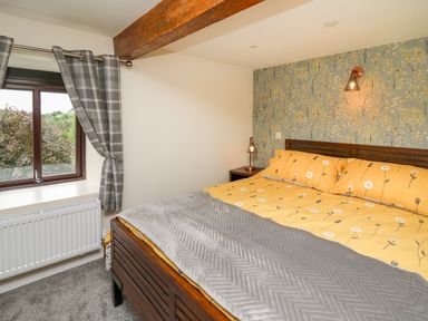 A bedroom with a bed yellow bedding gray blanket wooden headboard bedside table lamps window with checked curtains and radiator at Cwmfadog in Llanafan-fawr near Beulah