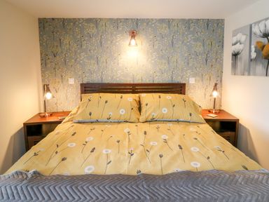 A bedroom with a bed with yellow floral bedding two bedside tables with lamps and floral wallpaper at Cwmfadog in Llanafan-fawr near Beulah