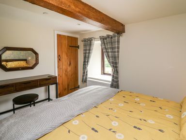 A bedroom with a yellow floral bedspread wooden door gray plaid curtains and a wooden dressing table with mirror at Cwmfadog in Llanafan-fawr near Beulah