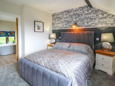 A bedroom with a large bed two bedside tables with lamps wallpaper behind the bed and a doorway leading to a bathroom at Cwmfadog in Llanafan-fawr near Beulah