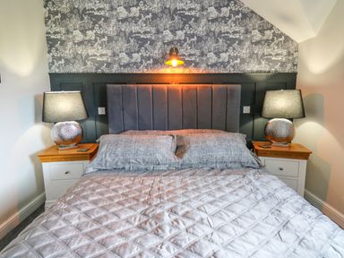 A bedroom with a bed centered between two nightstands with lamps and patterned wallpaper at Cwmfadog in Llanafan-fawr near Beulah