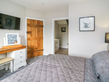 A bedroom with a bed grey bedding wooden door white desk with mirror TV on wall and door to bathroom at Cwmfadog Llanafan-fawr near Beulah