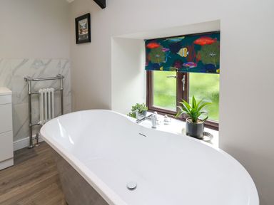 A bathroom with a white freestanding bathtub plants on the window sill and a colorful fish patterned window blind at Cwmfadog in Llanafan-fawr near Beulah