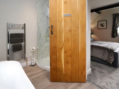 A bathroom with a wooden door labeled bathroom leading to a bedroom with a bed at Cwmfadog in Llanafan-fawr near Beulah