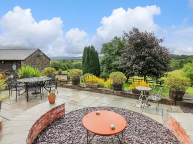 A garden patio with tables and chairs surrounded by plants and trees at Cwmfadog in Llanafan-fawr near Beulah