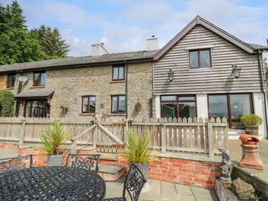 A stone and wood exterior house with a wooden fence and a metal patio table and chairs in the foreground at Cwmfadog in Llanafan-fawr near Beulah