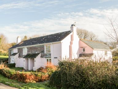 A cottage with a slate roof and pink walls surrounded by shrubs at 2 Rose Cottages Lansallos near Polperro