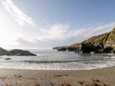 A rocky beach with small waves and hills in the background at 2 Rose Cottages Lansallos near Polperro