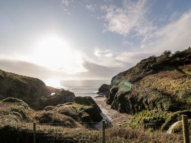 A coastal view with cliffs and a small beach at 2 Rose Cottages in Lansallos near Polperro