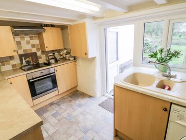 A kitchen with wooden cabinets a stove a sink and an open door to a garden at 2 Rose Cottages Lansallos near Polperro