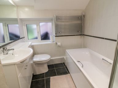 A bathroom with bathtub sink toilet towel radiator and frosted windows at 2 Rose Cottages Lansallos near Polperro