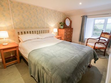 A bedroom with a double bed two bedside tables with lamps a chest of drawers a mirror a chair and a window at 2 Rose Cottages Lansallos near Polperro