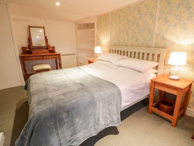 A bedroom with a double bed bedside tables lamps and a wooden dressing table at 2 Rose Cottages Lansallos near Polperro