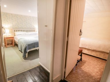 Two bedrooms visible through open doors one with a bed a side table and lamp and the other with a bed and a stool at 2 Rose Cottages Lansallos near Polperro